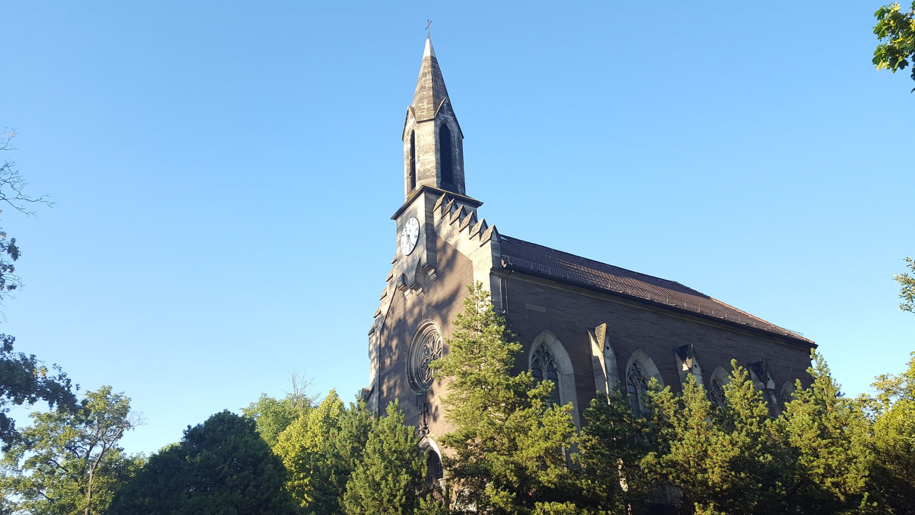 Neugotische Friedhofskapelle mit Uhrturm, Spitzbogenfenstern und Rosette im Sonnenlicht auf Hauptfriedhof Würzburg