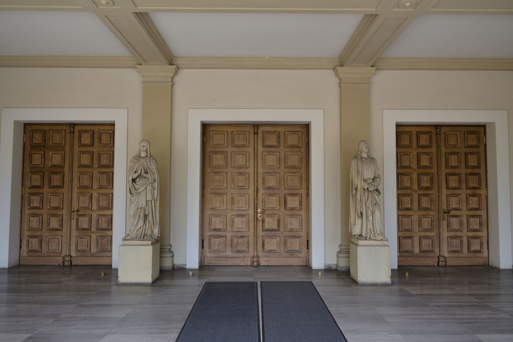Symmetrische Vorhalle der Aussegnungshalle mit drei Holztüren und Steinfiguren auf Hauptfriedhof Würzburg